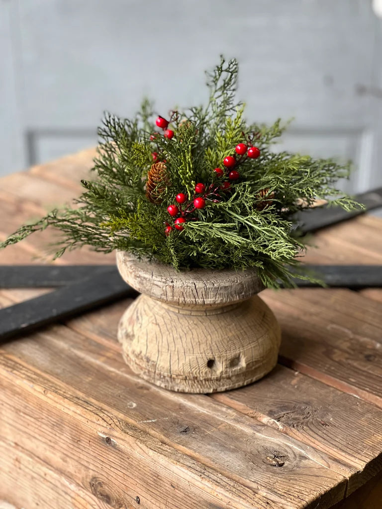 Decorative arrangement of greenery and red berries in a wooden container on a wooden surface.