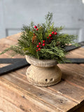 Decorative arrangement of greenery and red berries in a wooden container on a wooden surface.