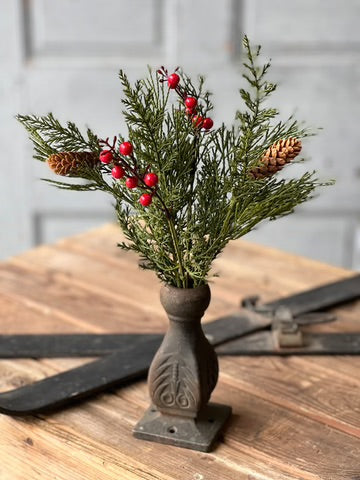 Decorative arrangement with greenery, red berries, and pinecones on a rustic wooden surface.