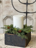 White candle in a wooden holder with greenery on a rustic surface