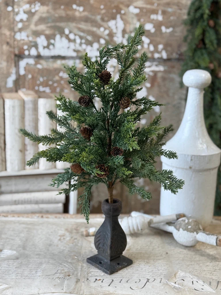 Small mixed evergreen stem with pinecones in a spindle shaped vase on a rustic wooden surface