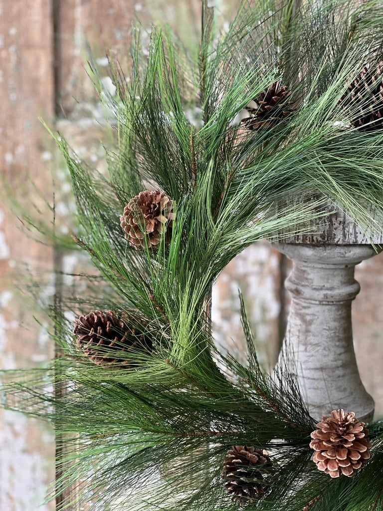 Decorative wreath close up of green pine branches and pinecones on a wooden surface.