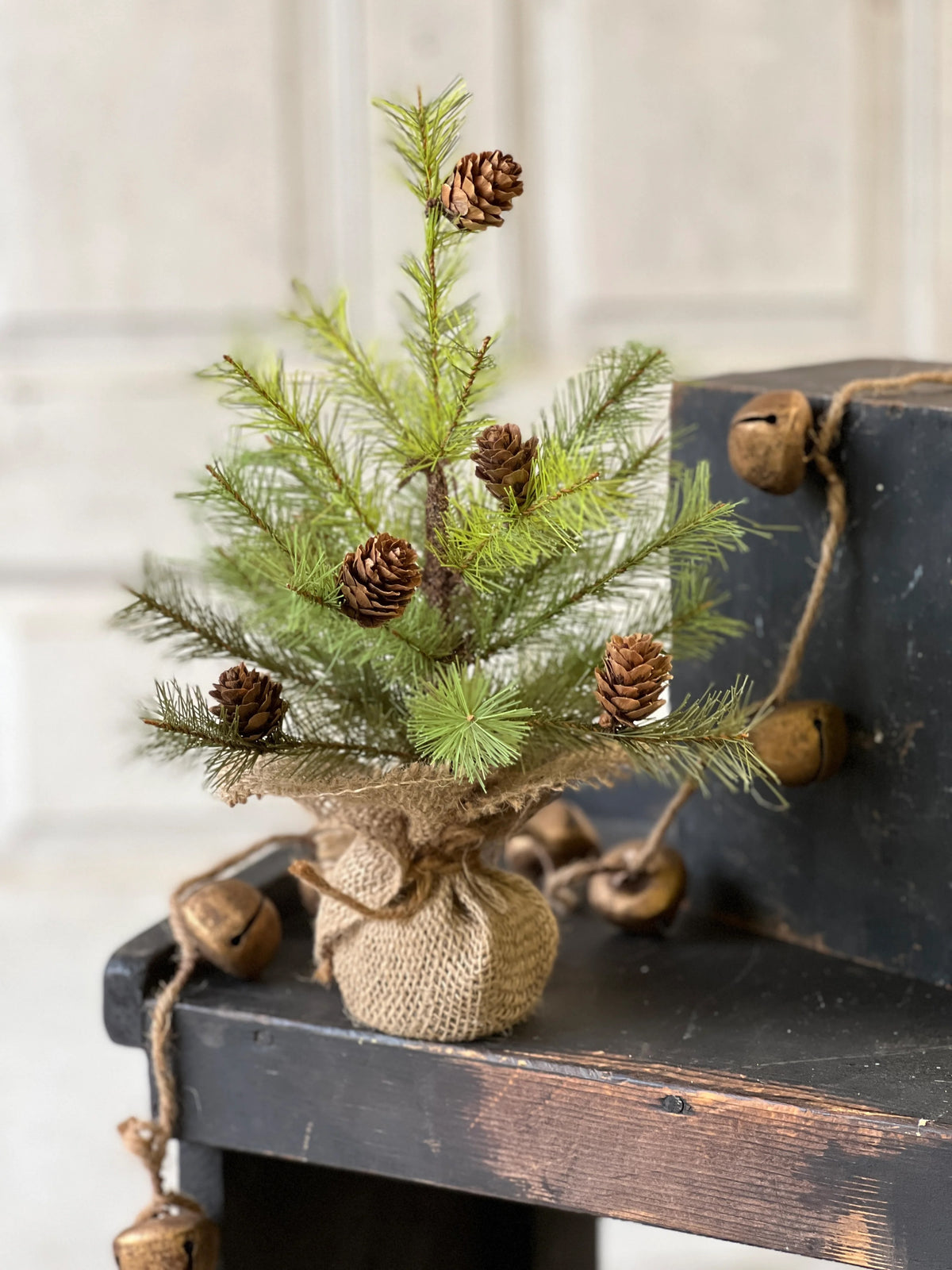 Small artificial Christmas tree with pinecones on a rustic wooden surface.