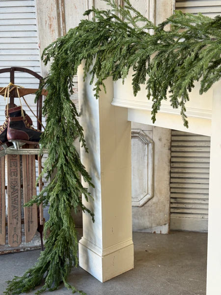 Green garland draped over a fireplace mantle with a rustic background.