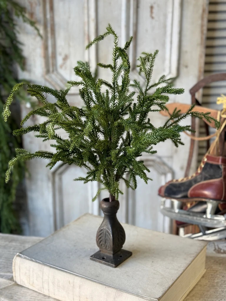Faux evergreen greenery in a decorative vase on a book with a vintage chair in the background