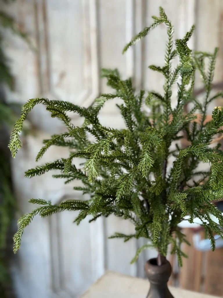 Evergreen faux stem in a vase on a table with a blurred background