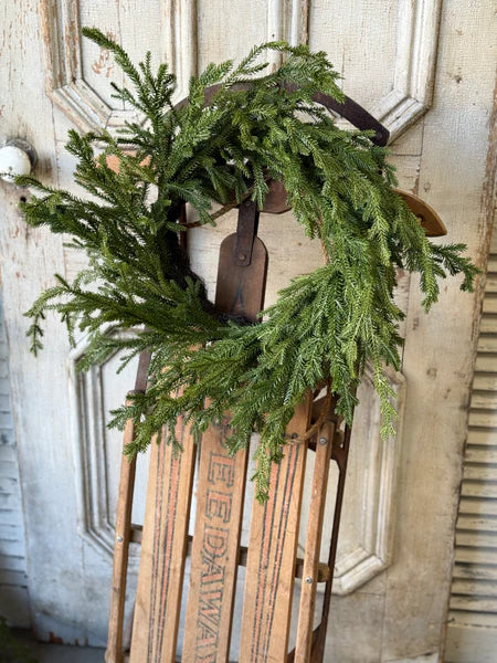 Green wreath on a wooden sled against a rustic wooden background