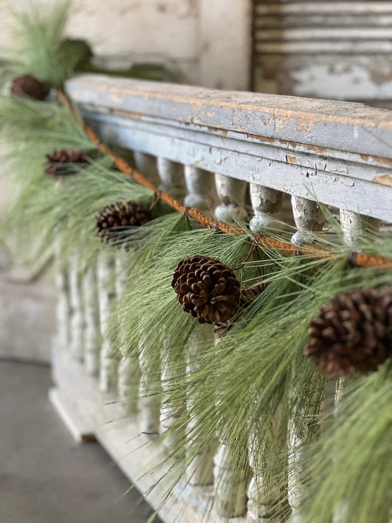 Decorative mantel with pine garland greenery and pinecones against a rustic wooden background