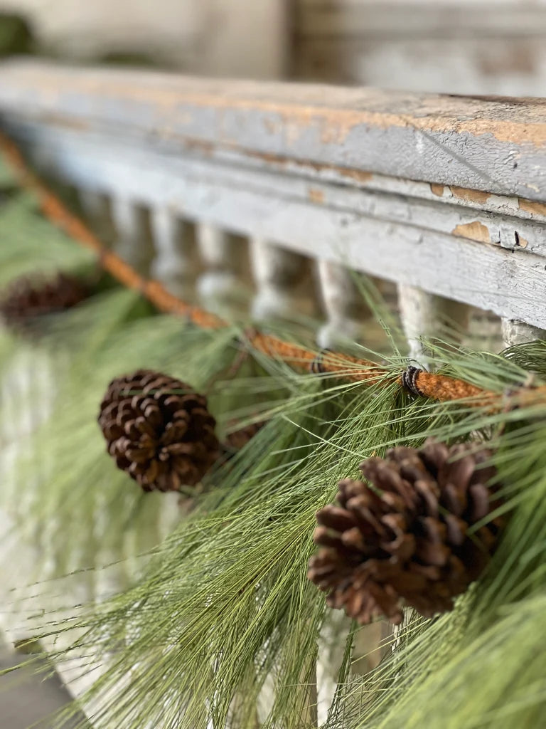 Decorative mantel with pine garland greenery and pinecones against a rustic wooden background