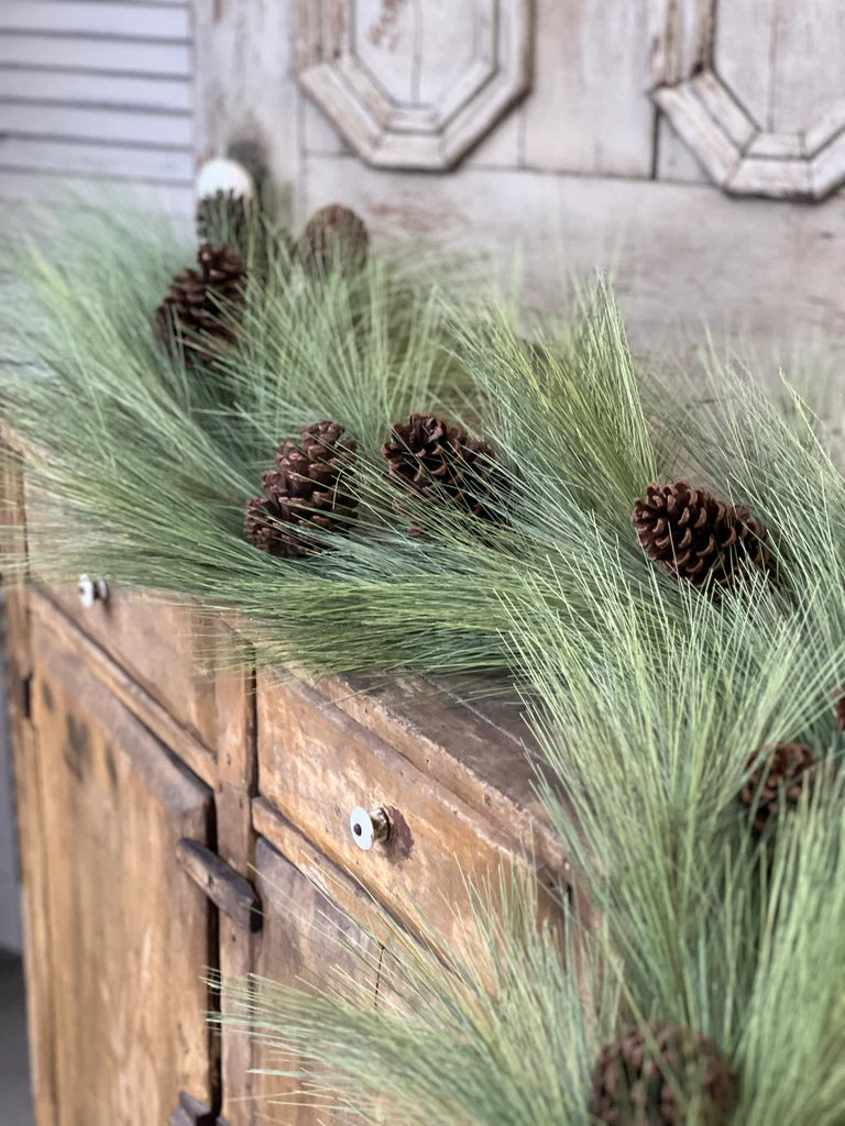 Close up of decorative pine garland with pinecones on a wooden surface