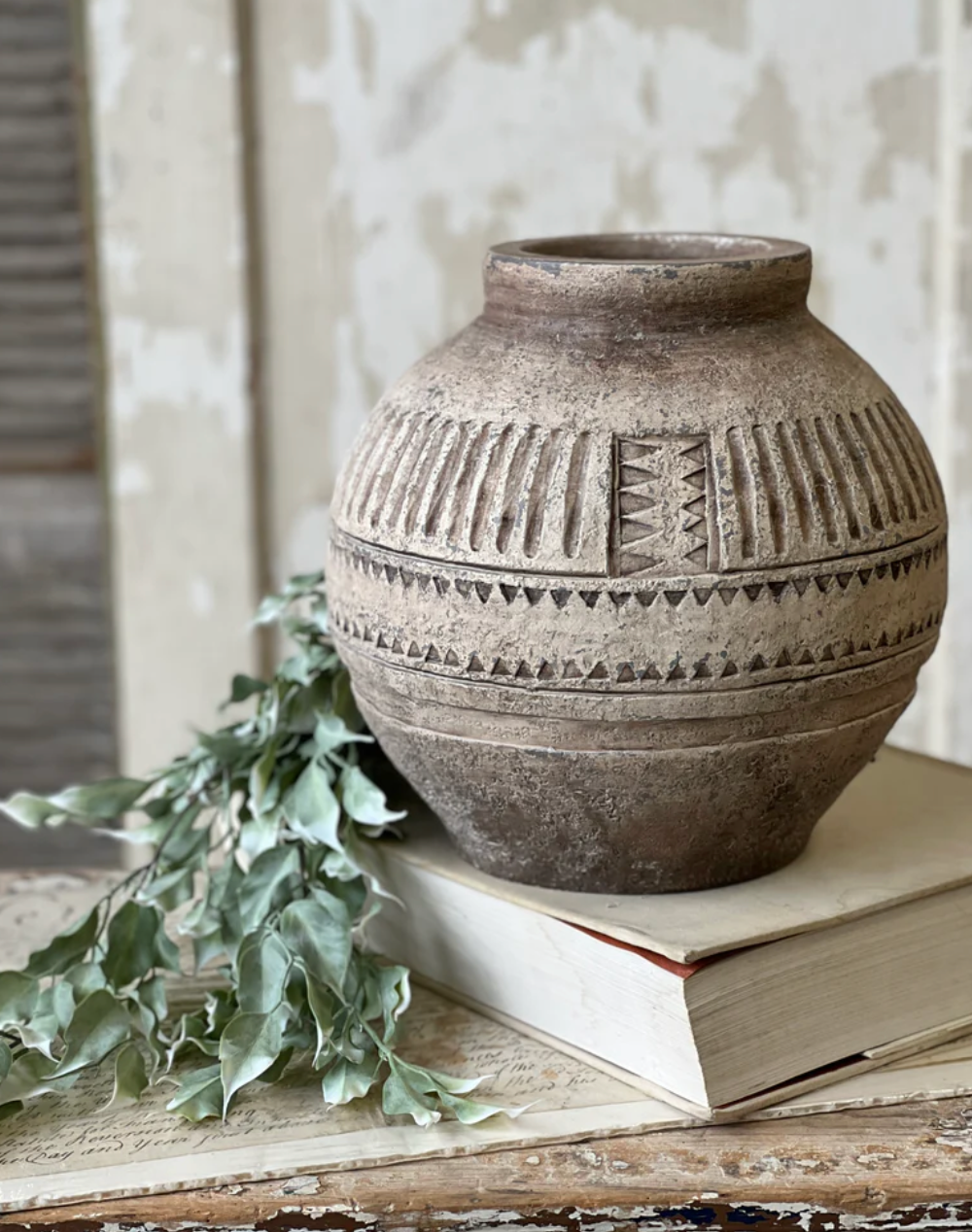 Decorative terracotta vase with geometric patterns on a wooden surface with books and greenery.