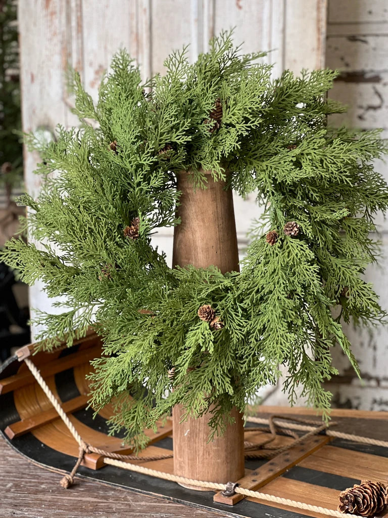 Green wreath with pinecones on a wooden stand against a rustic background