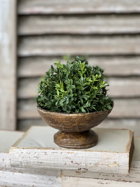 Green artificial boxwood half sphere in a wooden bowl on a white surface with a wooden background