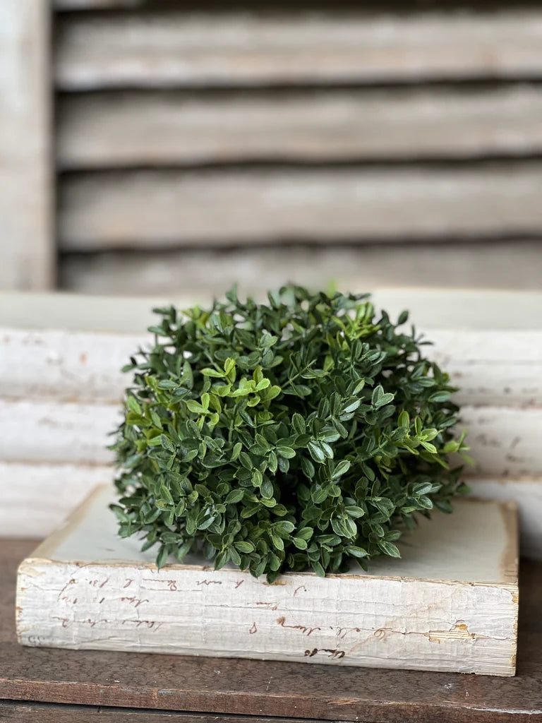 Faux green boxwood half sphere on a wooden box on a wooden surface with a wooden slatted background