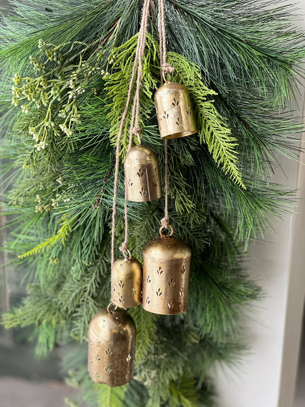 Decorative arrangement of greenery with hanging brass bells.