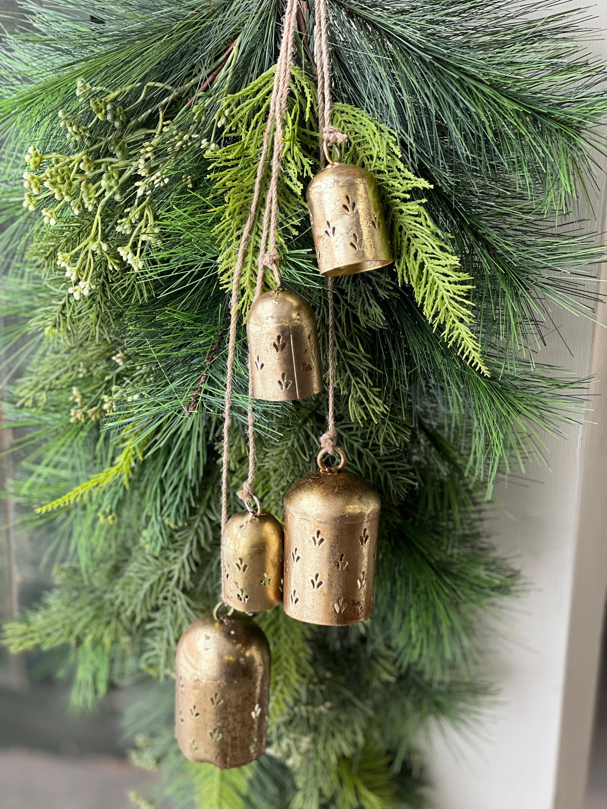 Decorative arrangement of greenery with hanging brass bells.