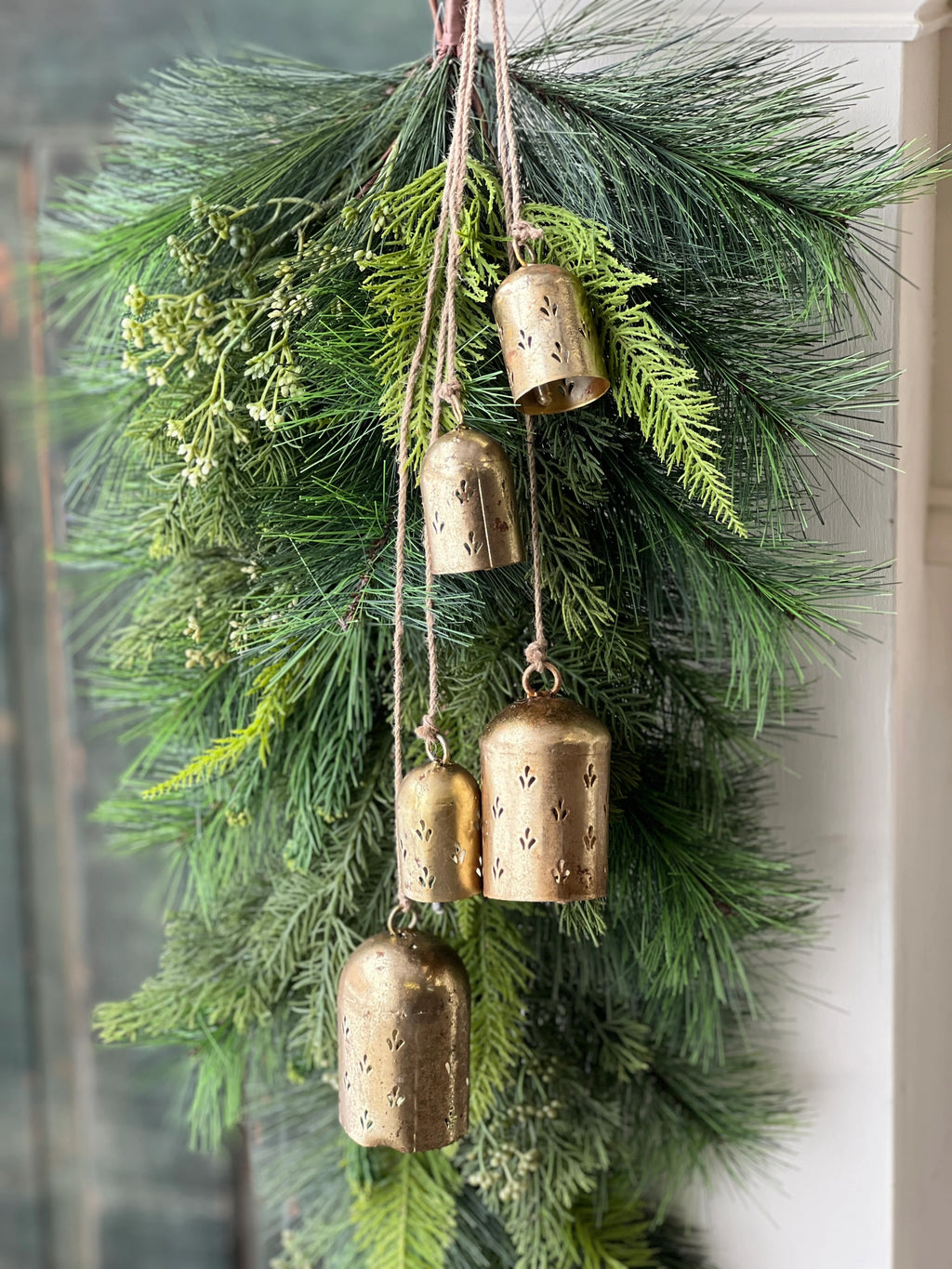 Decorative arrangement with greenery and gold bells hanging from a string.