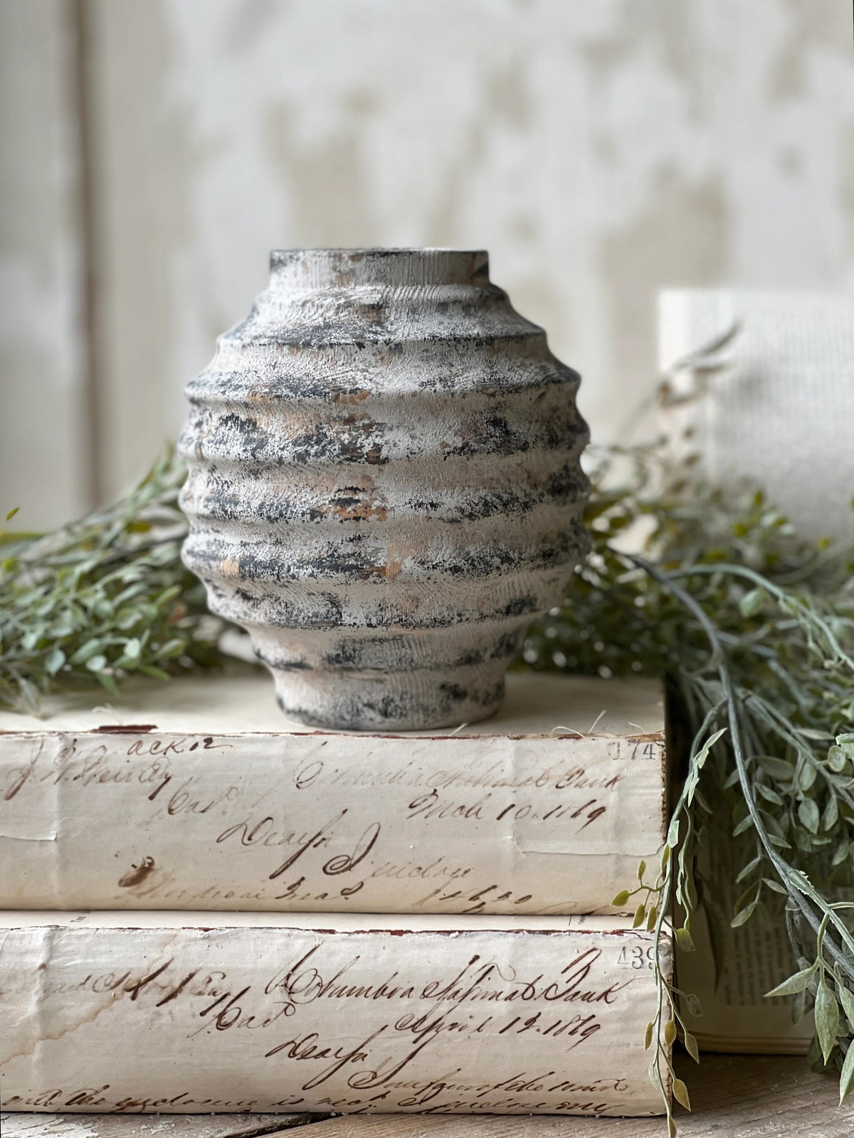 Textured ridged small wood vase with a distressed white wash finish over a dark bacground.  Vase is accented with greenery and sets on a stack of ivory colored books.