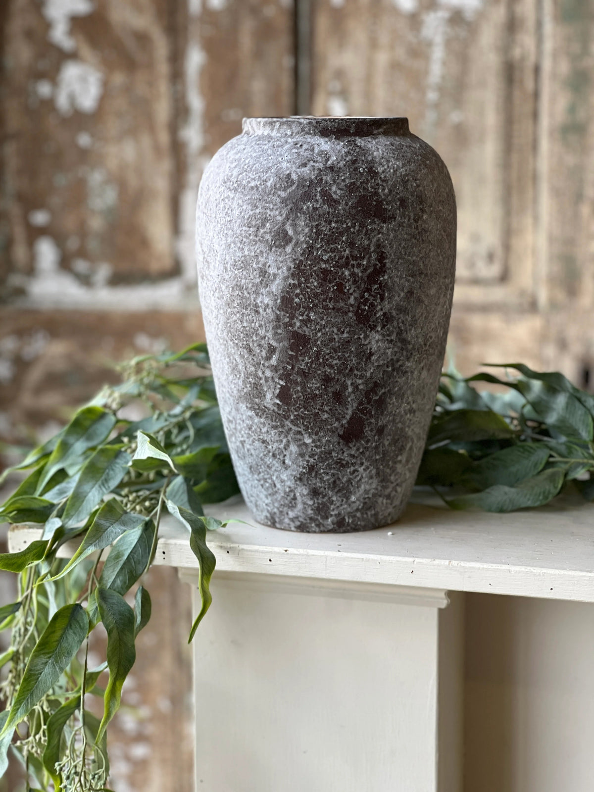 Textured red mottled vase on a white pedestal with green leaves in a rustic setting