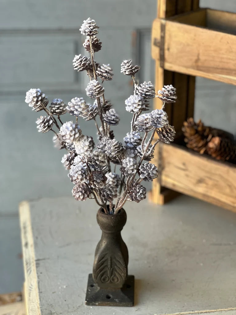 Decorative faux stem with pine cones in a rustic vase on a wooden surface.