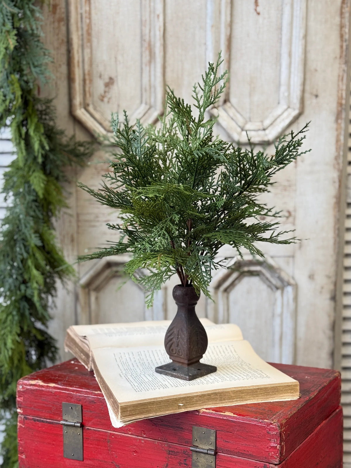 Artificial greenery stem in a wooden vase on an open book with a decorative background