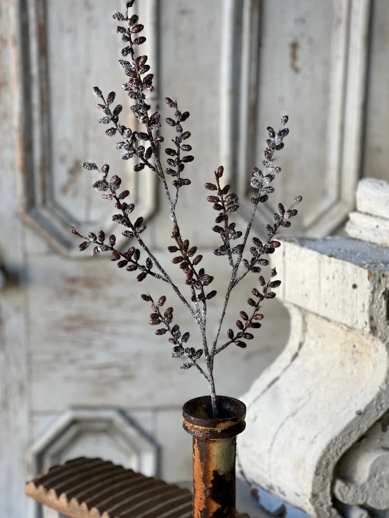 Decorative branch with small pod shaped berries in a rustic vase against a wooden background