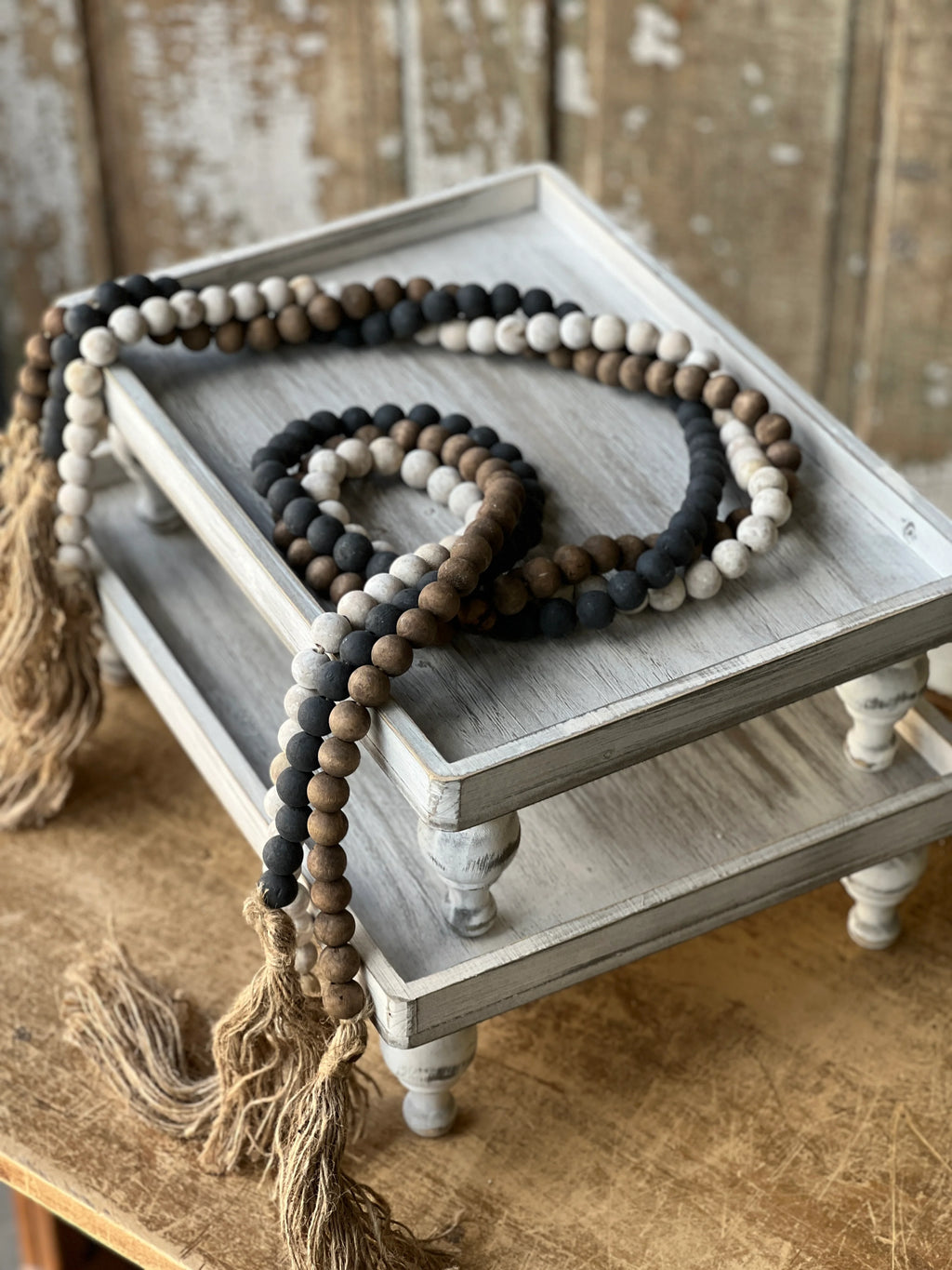 Wooden beaded garlands in black, white wash and natural wood tone with tassels on a wooden tray against a rustic background