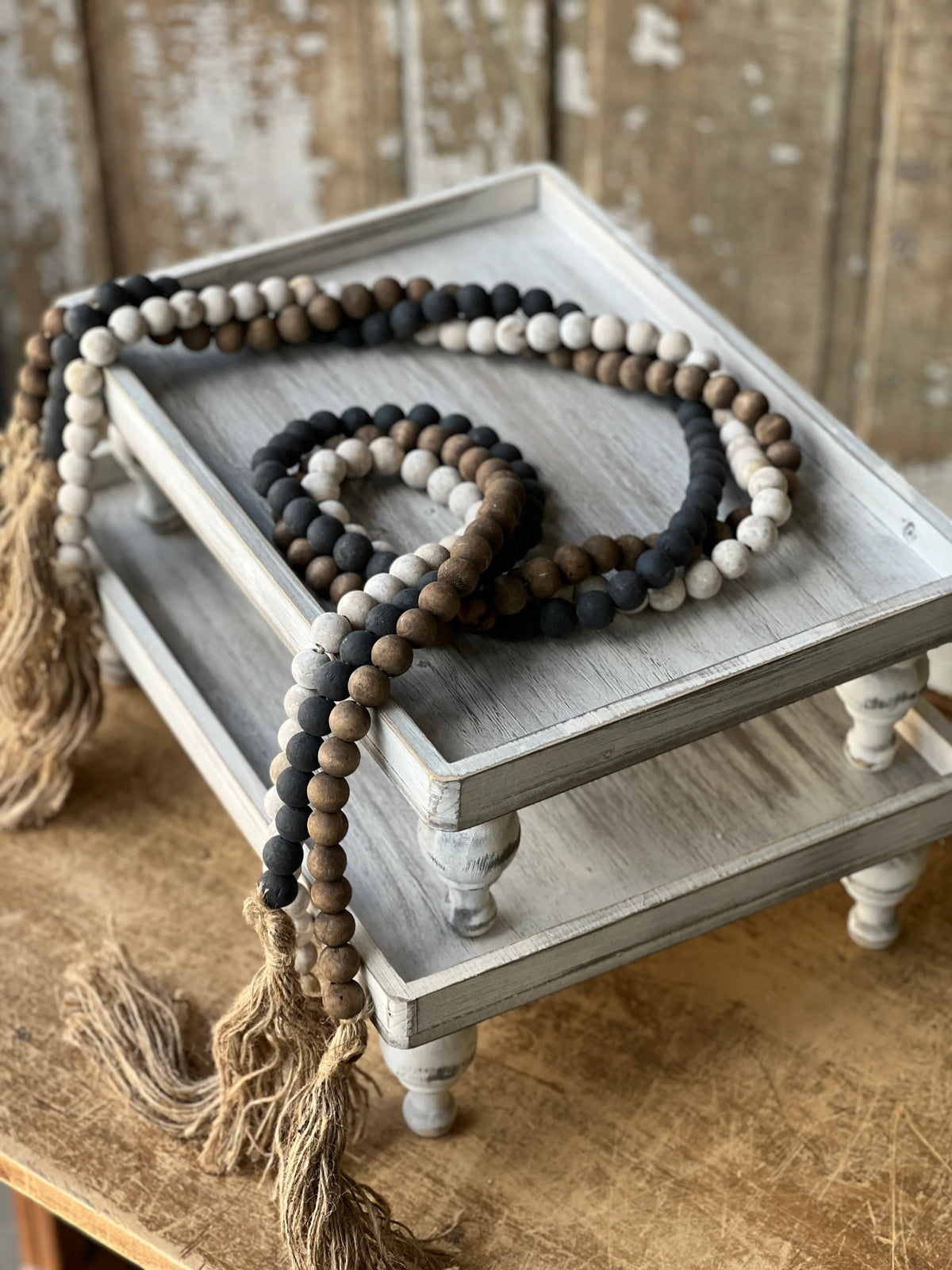 Wooden beaded garlands in black, white wash and natural wood tone with tassels on a wooden tray against a rustic background
