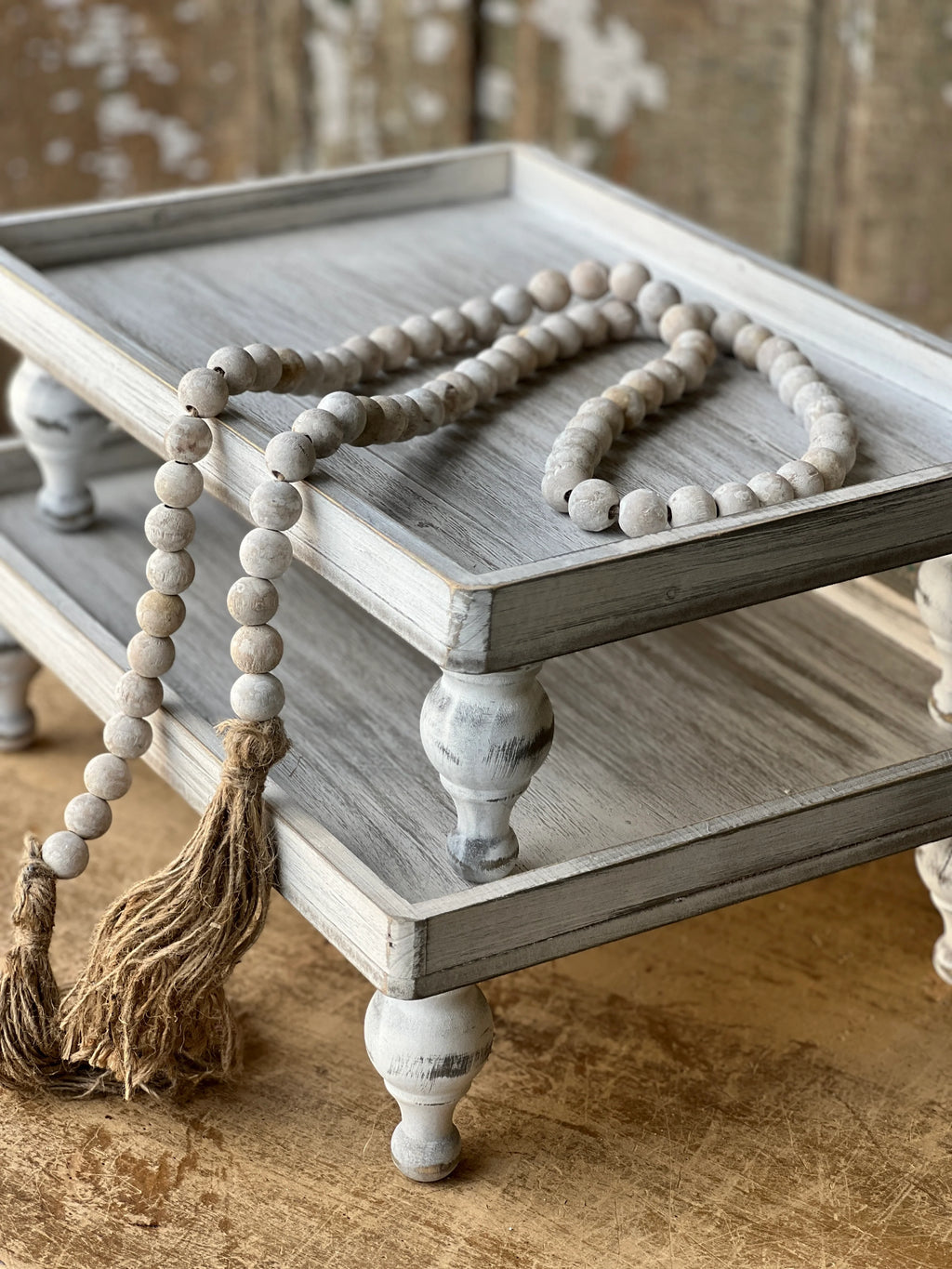 Wooden tray with decorative beaded garland and tassels on a rustic wooden surface