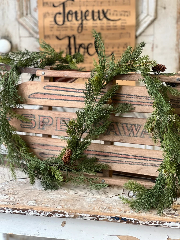 Wooden crate with green garland and a 'Joyeux Noel' sign in the background