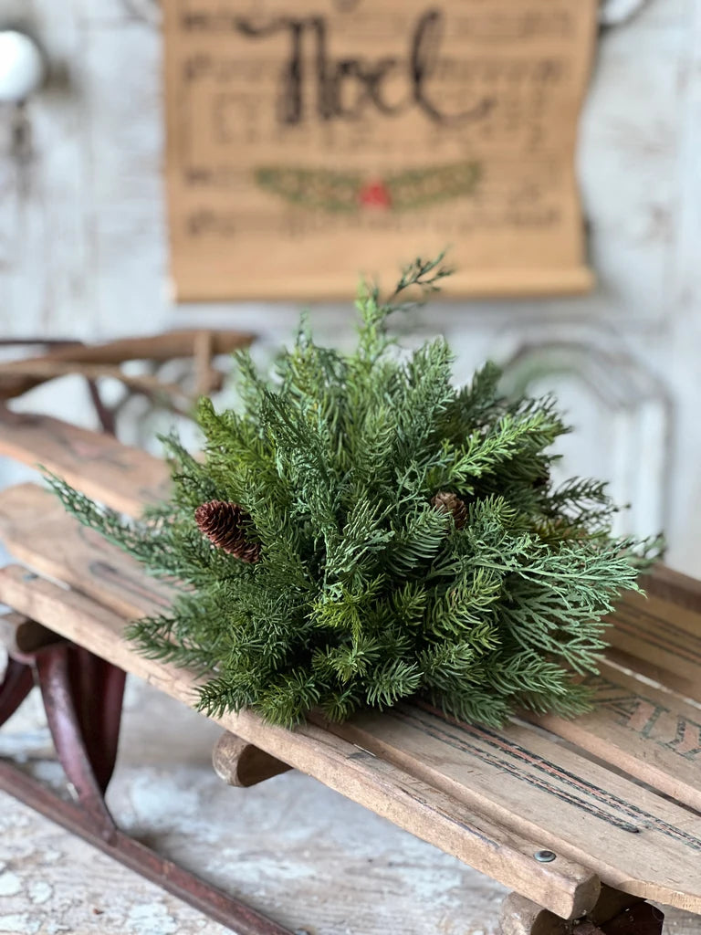 Evergreen half sphere greenery on a wooden bench with a 'Noel' sign in the background