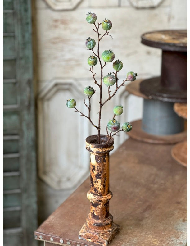 Decorative stem with green berry pods in a rustic metal vase on a wooden surface.