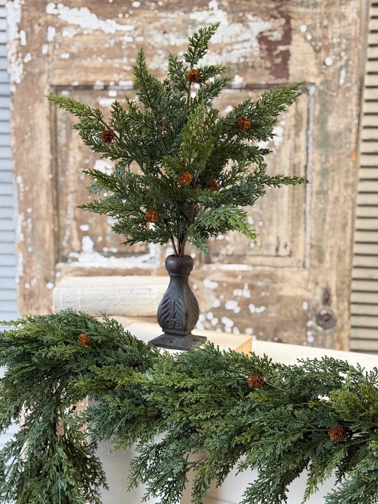 Decorative cedar evergreen stem with small orange berries in a dark vase on a mantel with a rustic background.
