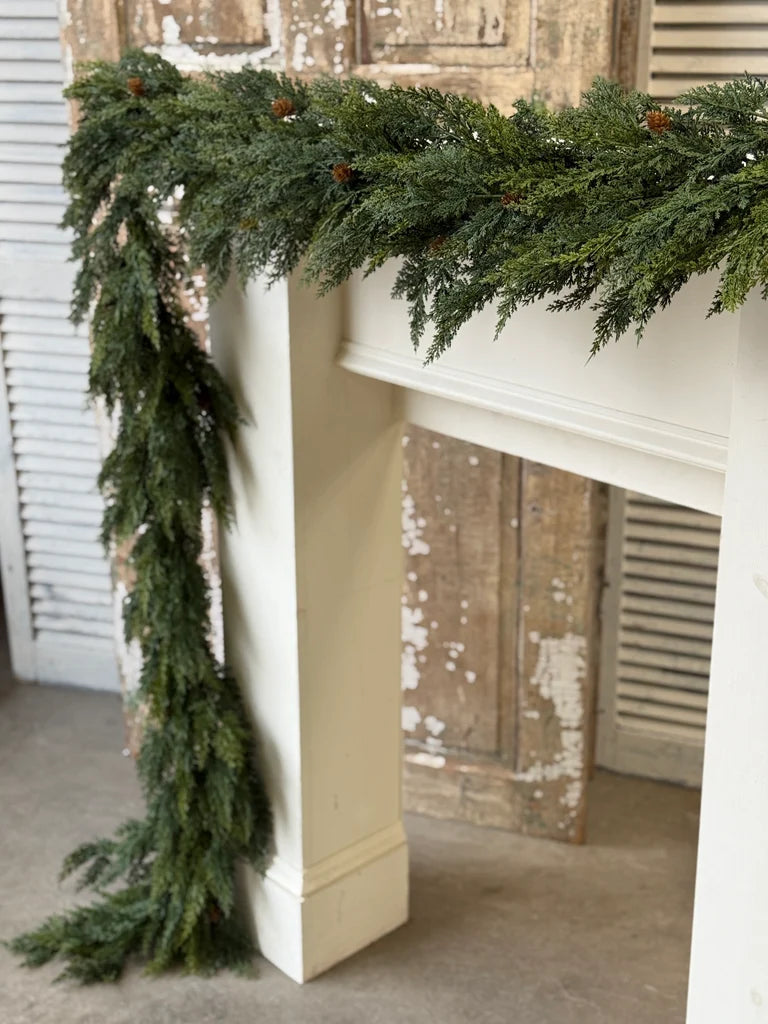 Green Christmas garland on a white fireplace mantel with a rustic wooden door in the background.