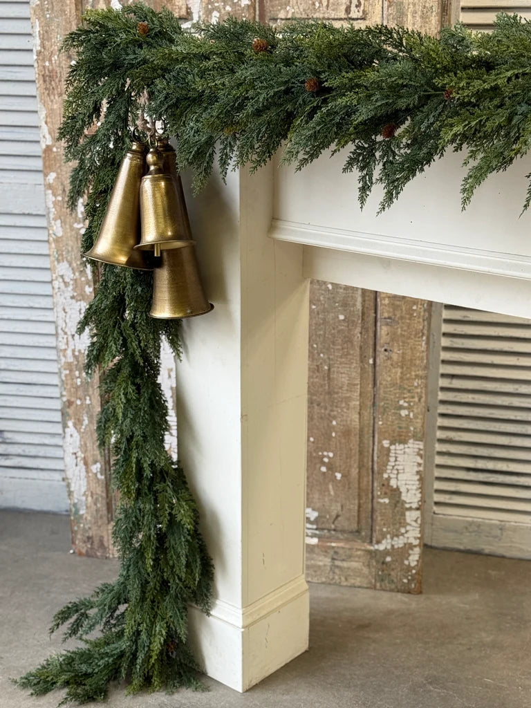 Decorative greenery with gold bells on a fireplace mantel.