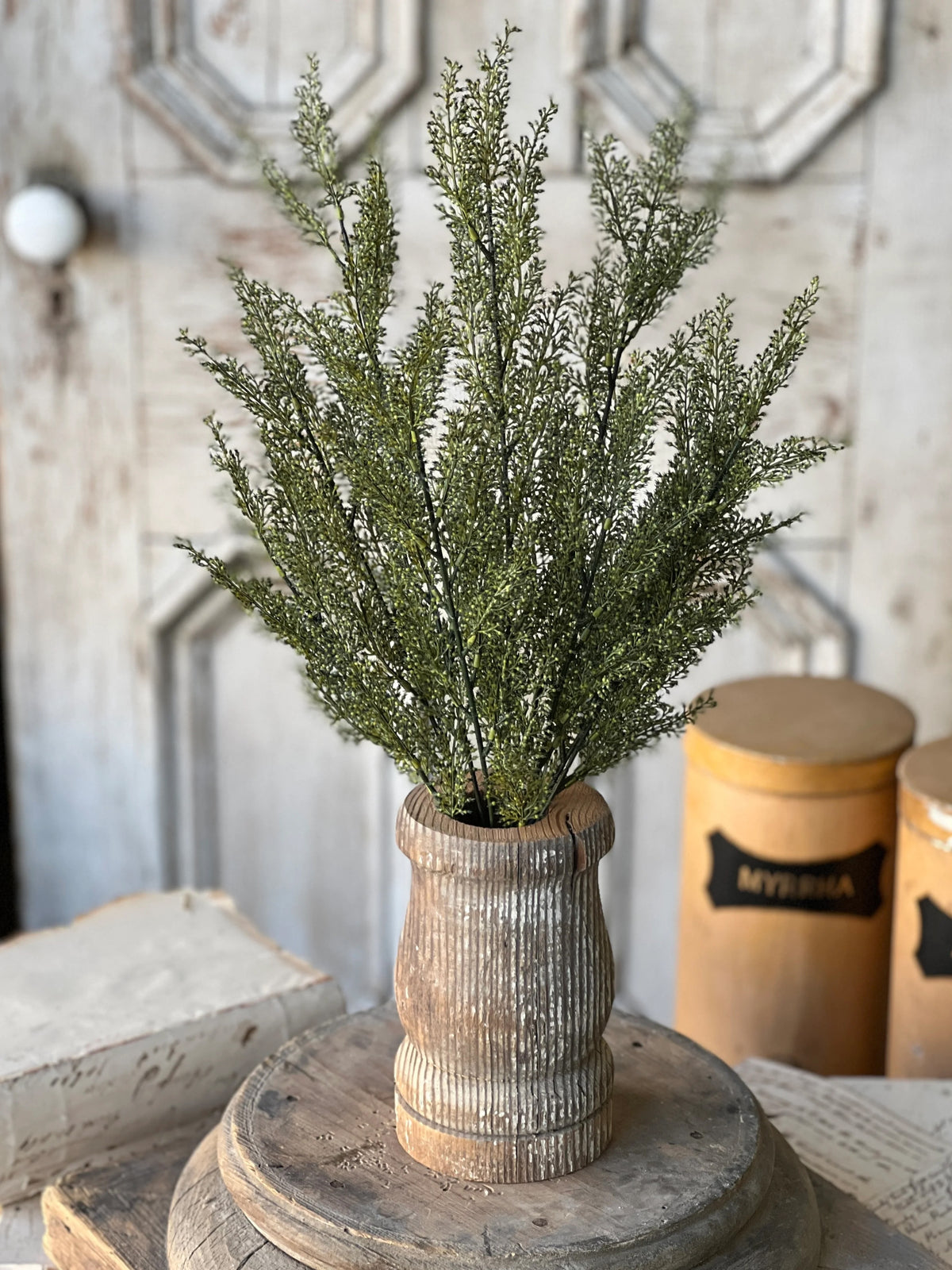 Faux greenery stem in a rustic wooden vase on a wooden surface with a neutral background